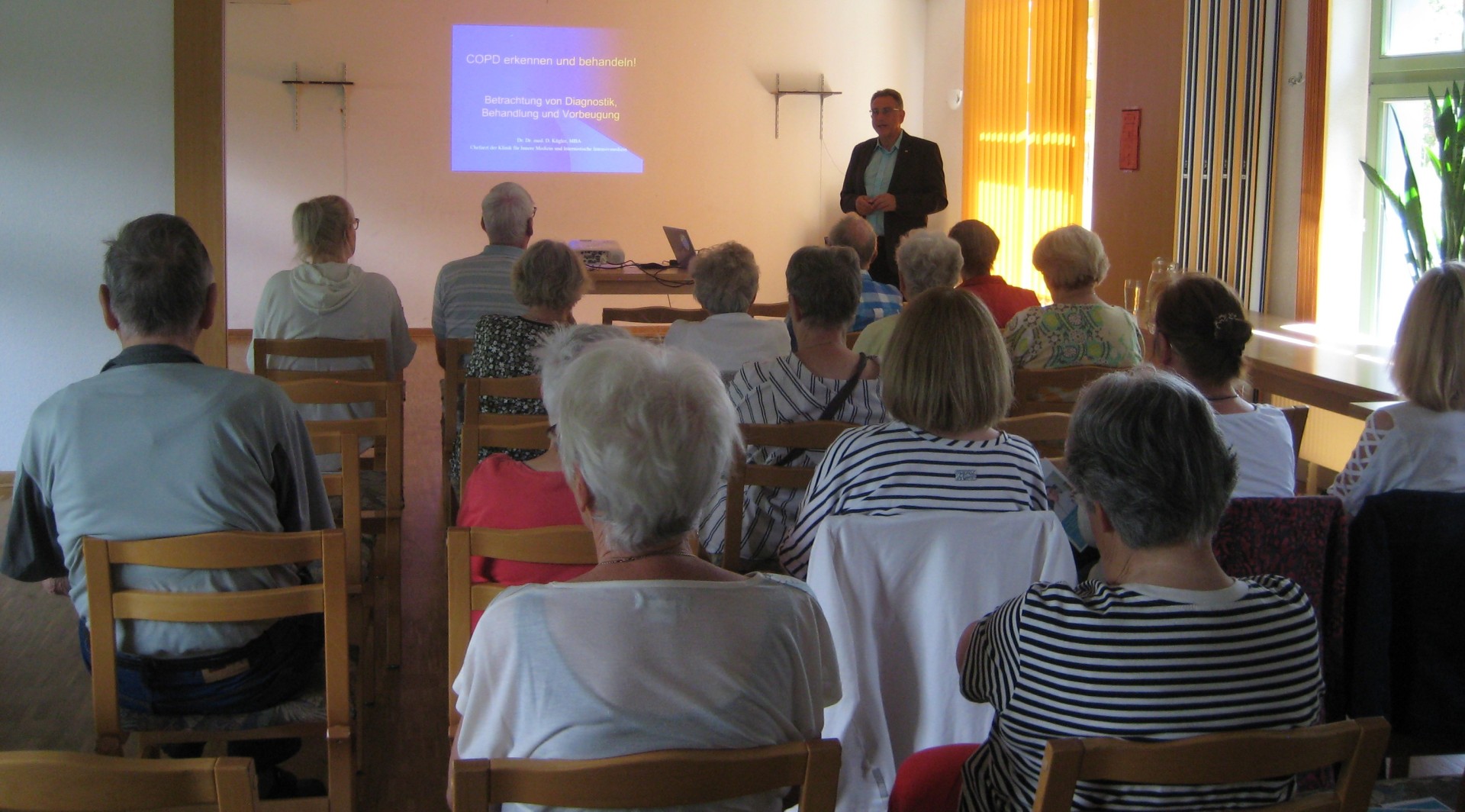 Besucher vor Leinwand während des Fachvortrages durch den Dr. Dr. med. Daniel Kügler, Chefarzt der Klinik für Innere Medizin und Internistische Intensivmedizin